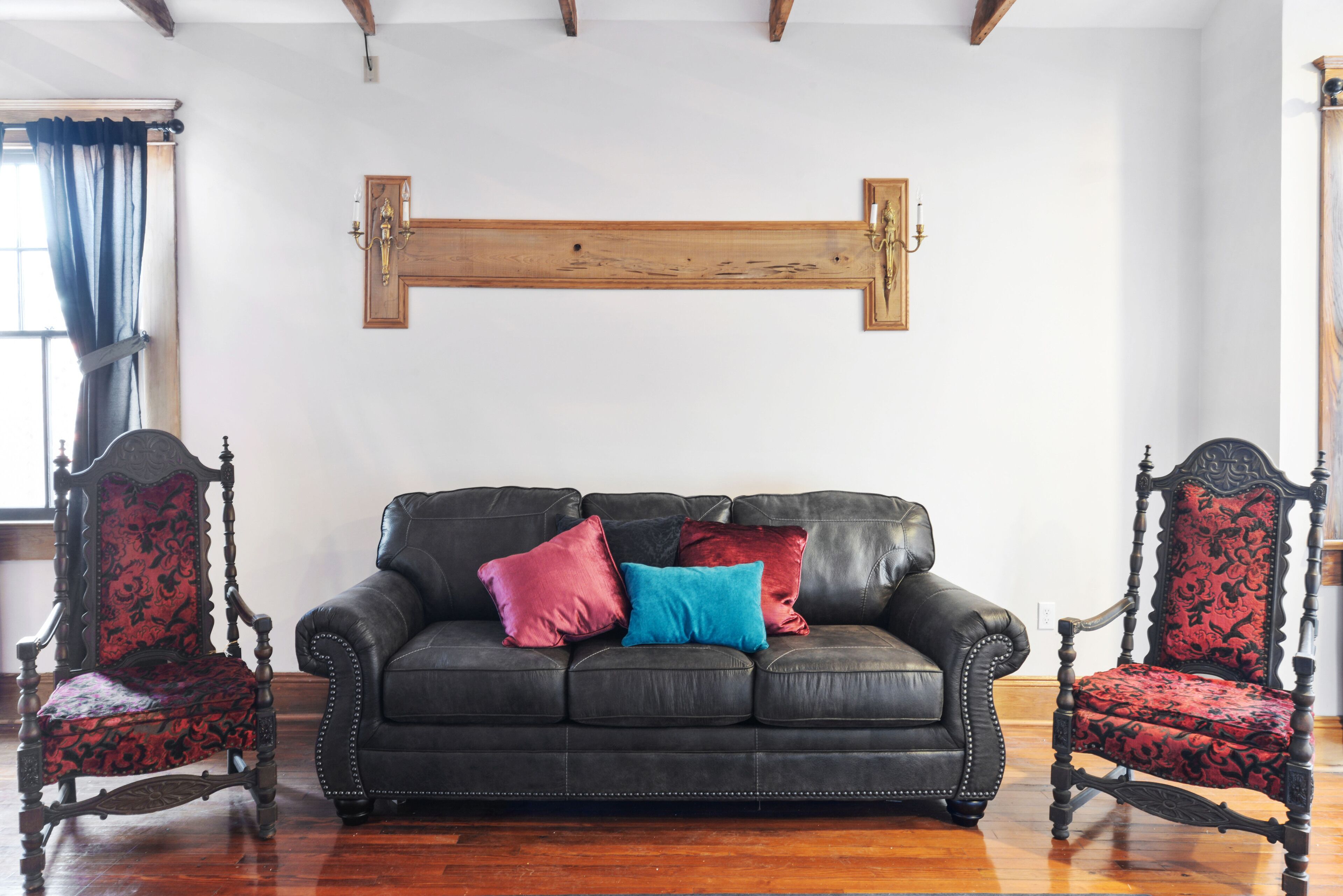 Una habitación con un sofá de cuero negro, dos sillones decorativos y una cruz de madera en la pared.