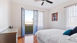 Une chambre à coucher comprenant un lit, une commode, un ventilateur de plafond et une porte donnant sur un balcon extérieur.
