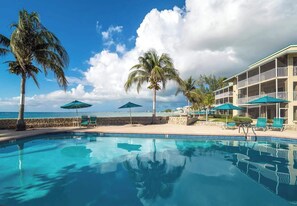 A pool area with clear blue water, palm trees, and a building with balconies.