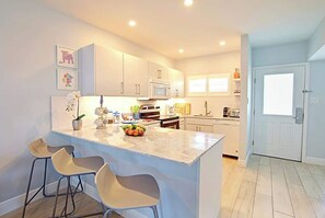 A modern kitchen with white cabinets, a marble island, and bar stools.