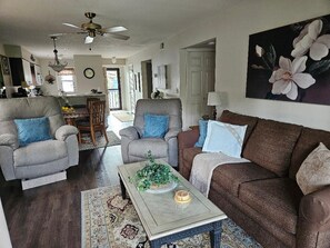 A living room with a ceiling fan, two sofas, a coffee table with a plant, and a painting on the wall.