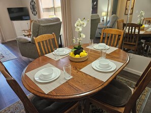 A dining area with a wooden table set for four, surrounded by chairs.