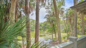 A view of a water body surrounded by tall trees, with a wooden deck in the foreground. - Walk to Beach! Remodeled Cottage on Sparrow Pond (Kiawah Island)