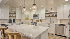 A modern kitchen with white cabinetry, a central island, pendant lighting, and stainless steel appliances. - Walk to Beach! Remodeled Cottage on Sparrow Pond (Kiawah Island)