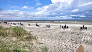 A beach with rows of beach chairs and umbrellas, a sandy shore, and a cloudy sky. - Walk to Beach! Remodeled Cottage on Sparrow Pond (Kiawah Island)