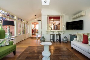 A spacious living area with a green sofa, a white armchair, a white coffee table, and a TV mounted on the wall.
