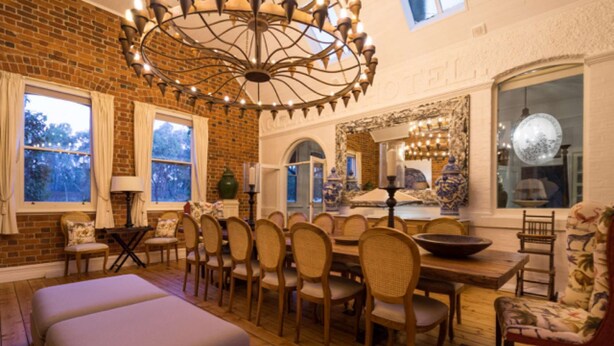 A dining area with a brick wall, wooden flooring, and a large chandelier. There are multiple chairs and a table with a bowl on it. - Rent your own Hotel in the Victorian Goldfields (Maldon)