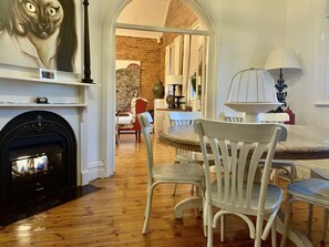 A cozy room with a fireplace, white chairs, a dining table, and a large painting.