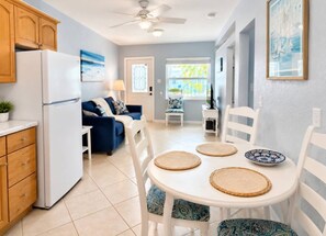 Een kleine keuken met een koelkast, houten keukenkastjes, een eettafel met placemats en een blauwe bank.