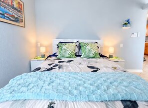 Een bed met een bloemenprint, twee nachtkastjes met lampen, een wandplank met bloemen en een schilderij aan de muur.