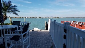 Eine Uferterrasse mit Außenbestuhlung, Blick auf das Wasser und eine entfernte Uferlinie mit Gebäuden.