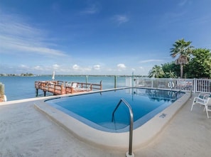 Ein Pool mit Blick auf das Wasser und eine Liegefläche mit Liegestühlen.