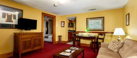 A hotel room with a red carpet, wooden furniture, a television, a dining area, and a painting on the wall.