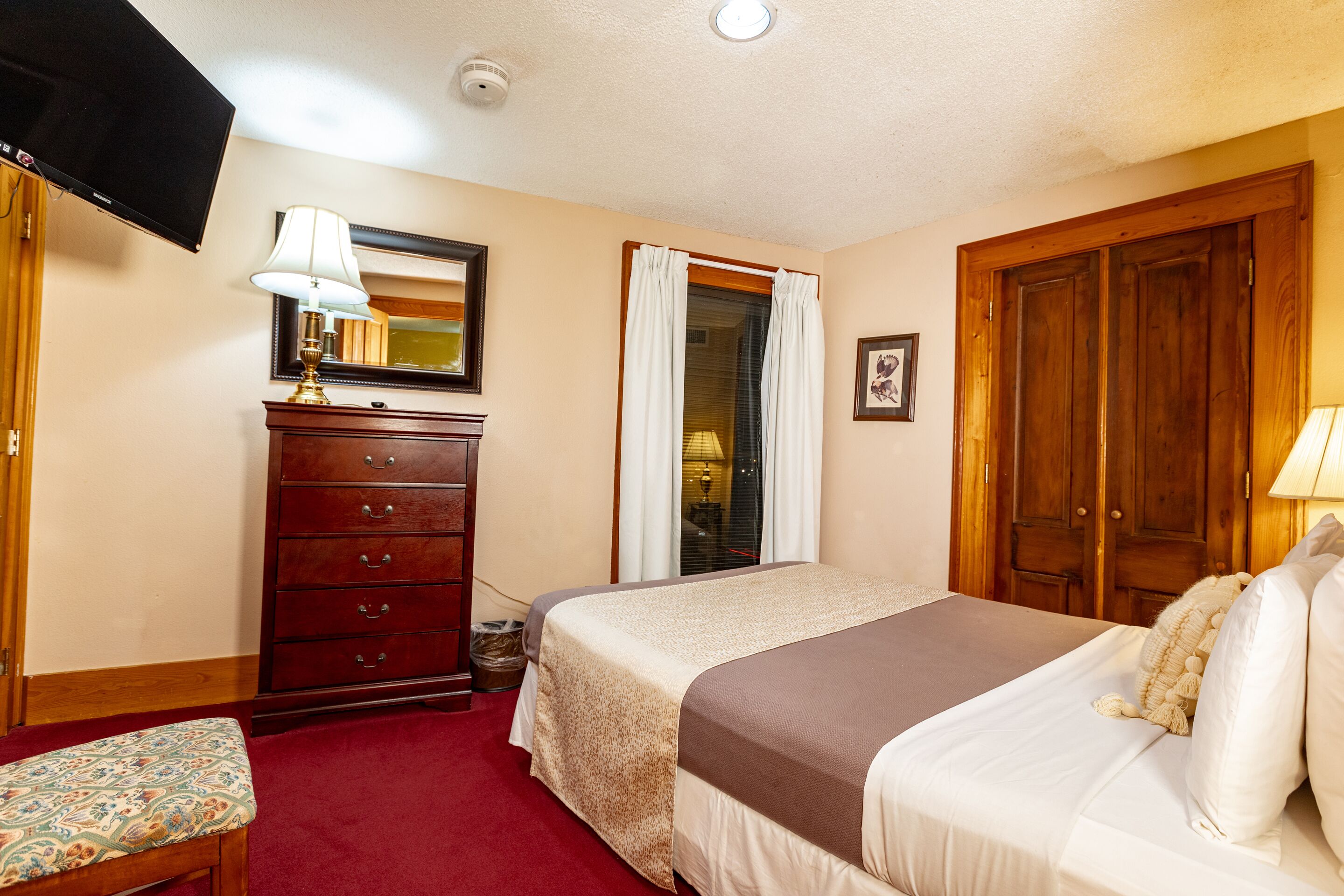 Une chambre d’hôtel avec un lit, une commode, une télévision et une fenêtre avec des rideaux.