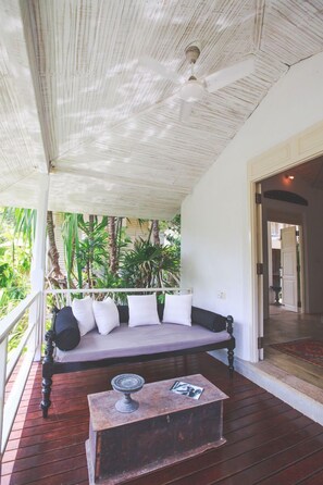 Une terrasse en bois avec un lit, un ventilateur de plafond et une table en pierre sur laquelle est posé un magazine.
