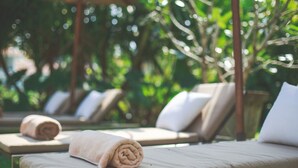 Une rangée de chaises longues dotées de coussins beige et d’oreillers blancs, une serviette enroulée sur l’une d’elles, et un auvent au-dessus.