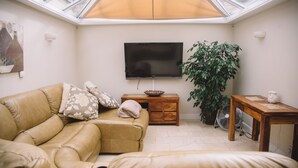 Un salón acogedor con sofá, televisión, mesita de madera, planta en maceta y tragaluz.
