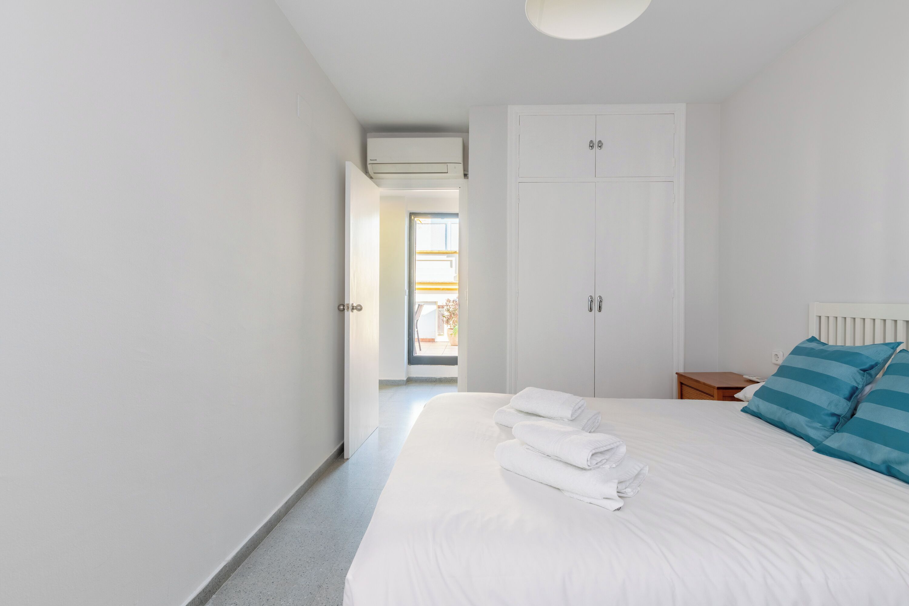A hotel room with a large bed, white walls, a wardrobe, and an air conditioning unit.