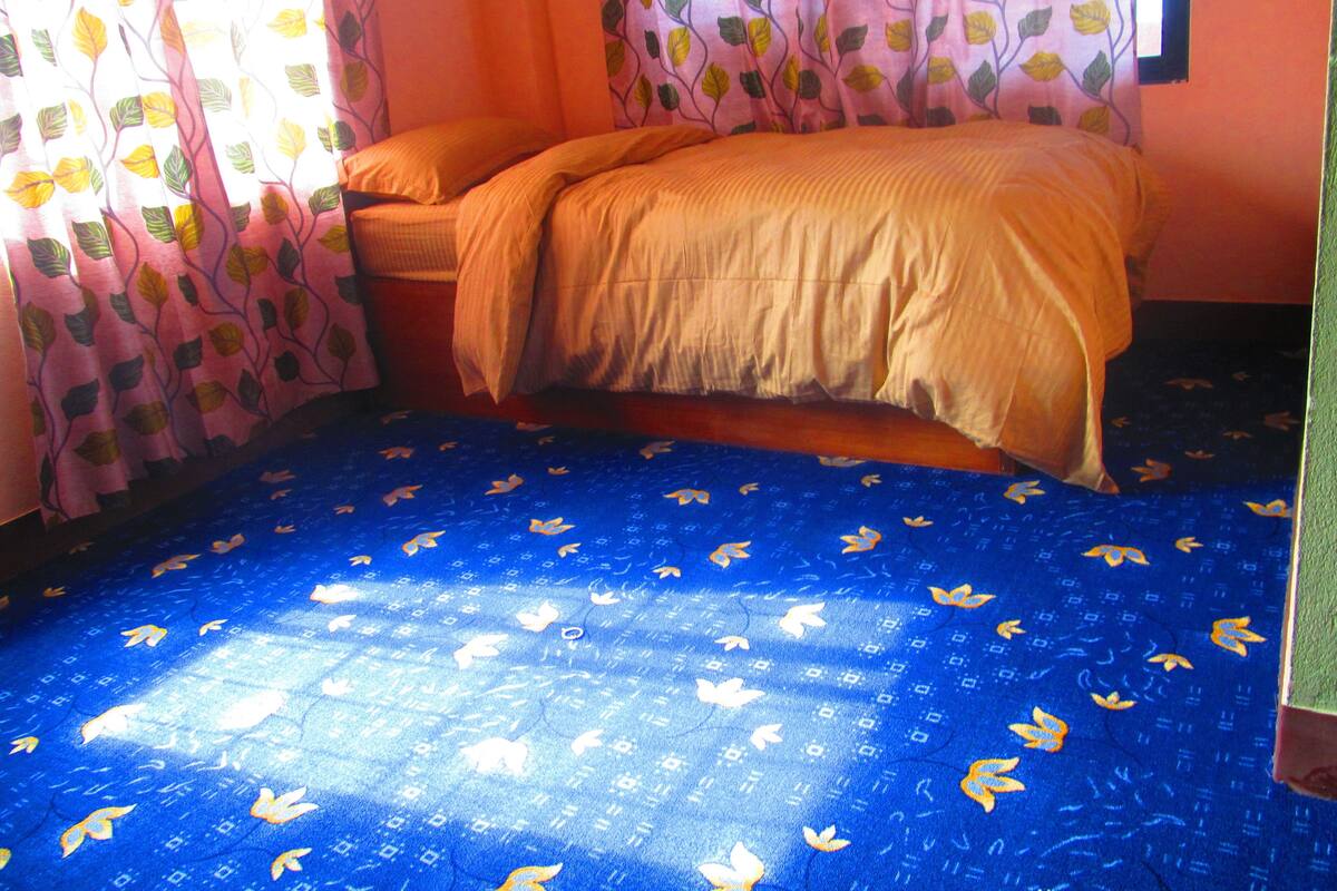 A room with a bed, a window with curtains, and a patterned blue carpet.
