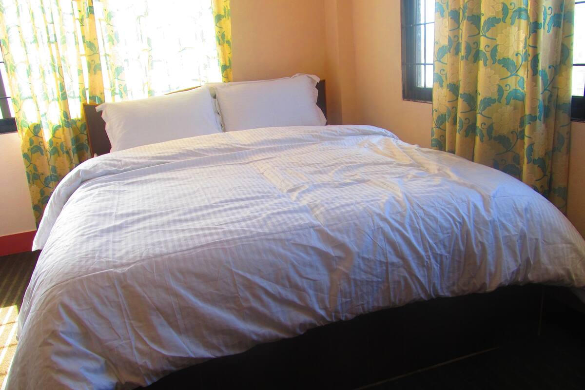 A neatly made bed in a room with floral curtains and a window.
