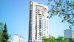 A tall, multi-story building with a modern design, surrounded by a grassy area and trees. - Apartment in Vitebsk Tower (Vitebsk)