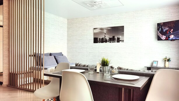 A modern living room with a dining area, featuring a sofa, a TV mounted on the wall, and a cityscape picture. - Apartment in Vitebsk Tower (Vitebsk)