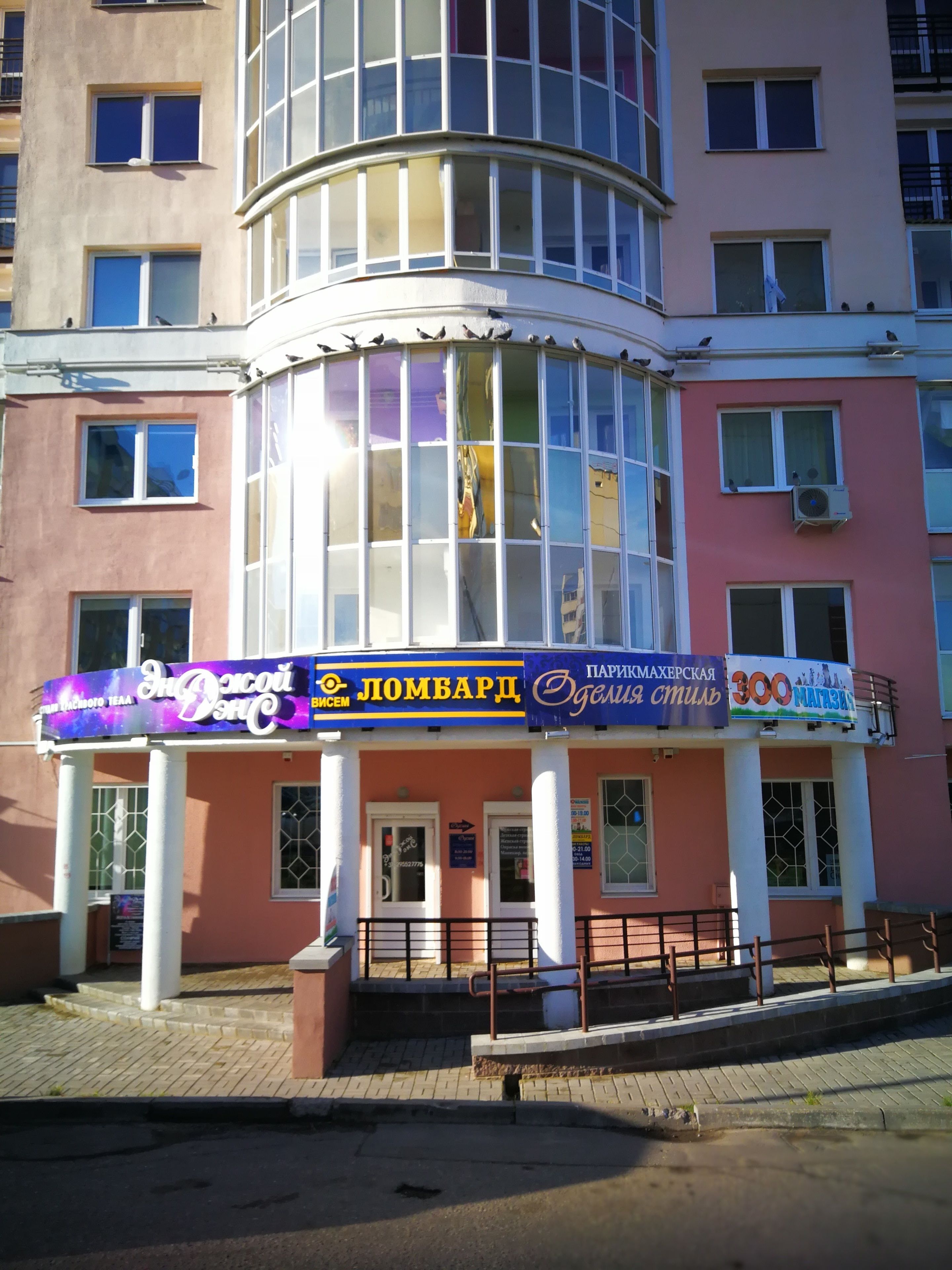 Un edificio con fachada de vidrio curva, múltiples ventanas y varios carteles que anuncian negocios.