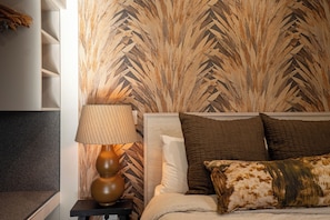 A bedroom with a bed, pillows, a nightstand, a lamp, and a wall with a geometric pattern. - Twizel Cottages (Twizel)