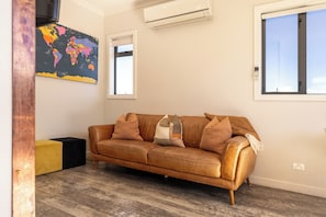 A modern living room with a brown leather sofa, a world map artwork, and a large window. - Twizel Cottages (Twizel)
