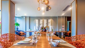 A dining area with a long wooden table set for a meal, surrounded by wicker chairs, and a modern chandelier overhead. - Courtyard Hotel – Li River Branch (Guilin)