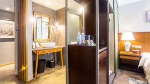 A hotel room with a wooden vanity, a large mirror, a bed with a white headboard, and a nightstand with a lamp. - Courtyard Hotel – Li River Branch (Guilin)