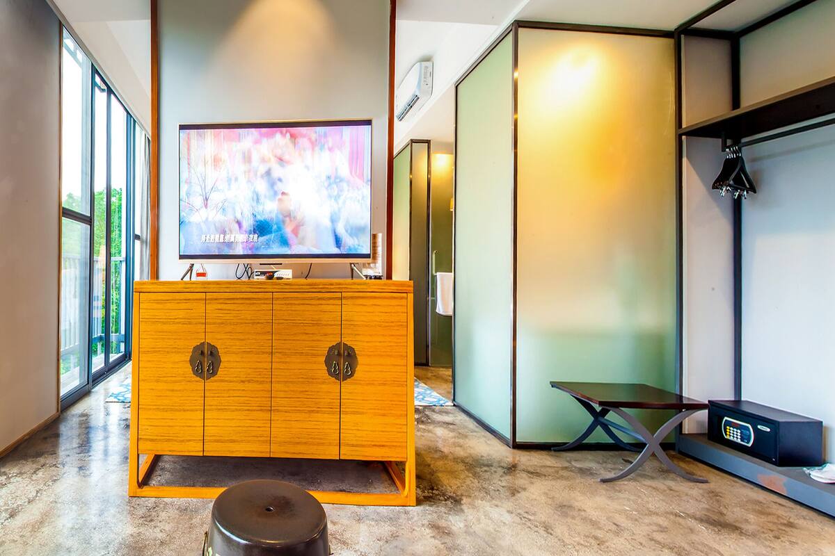 A modern bathroom with a wooden vanity, a large mirror, and a television.