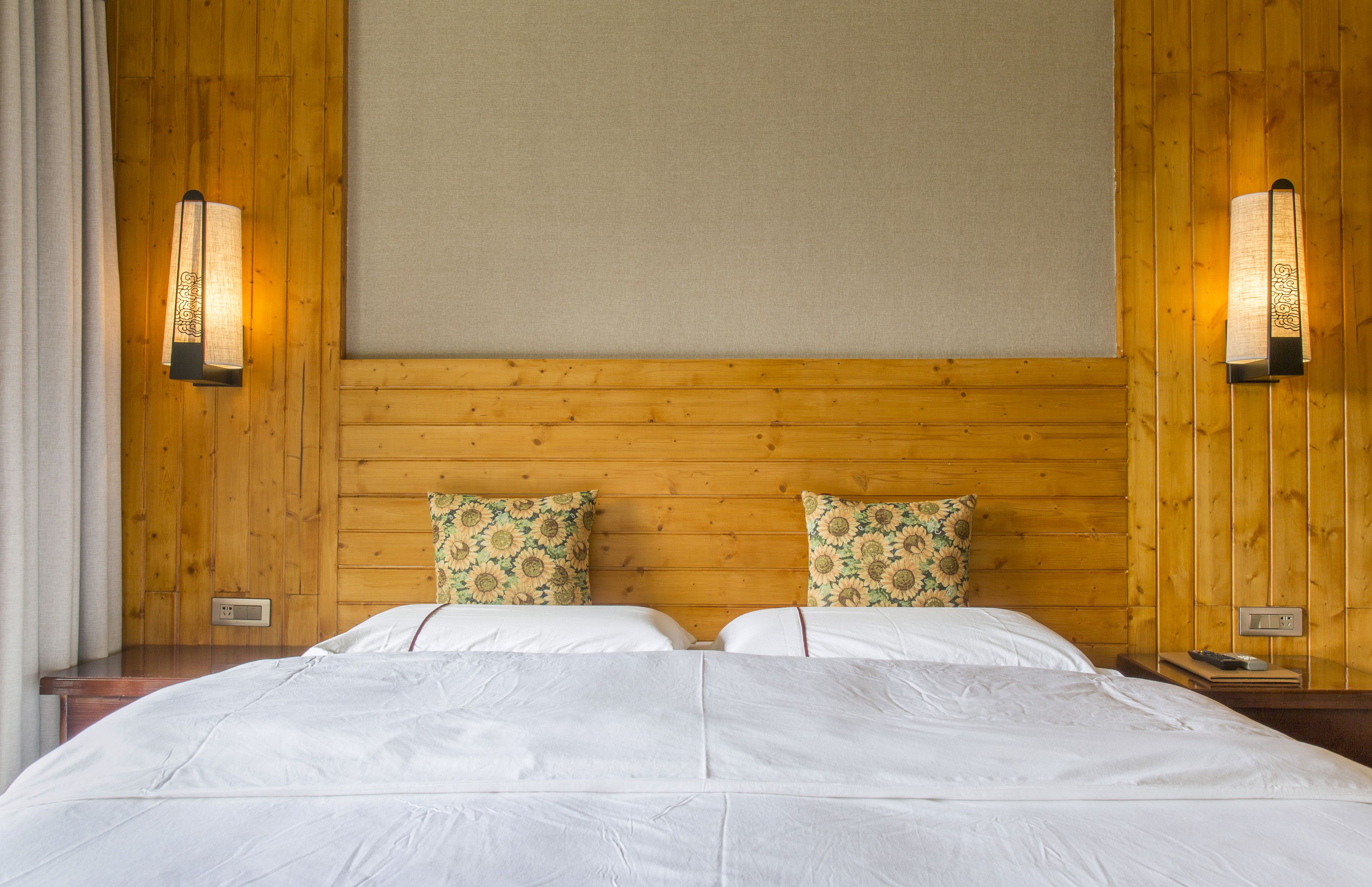 Een tweepersoonsbed met witte lakens, twee sierkussens met bloemendesign en houten lambrisering.