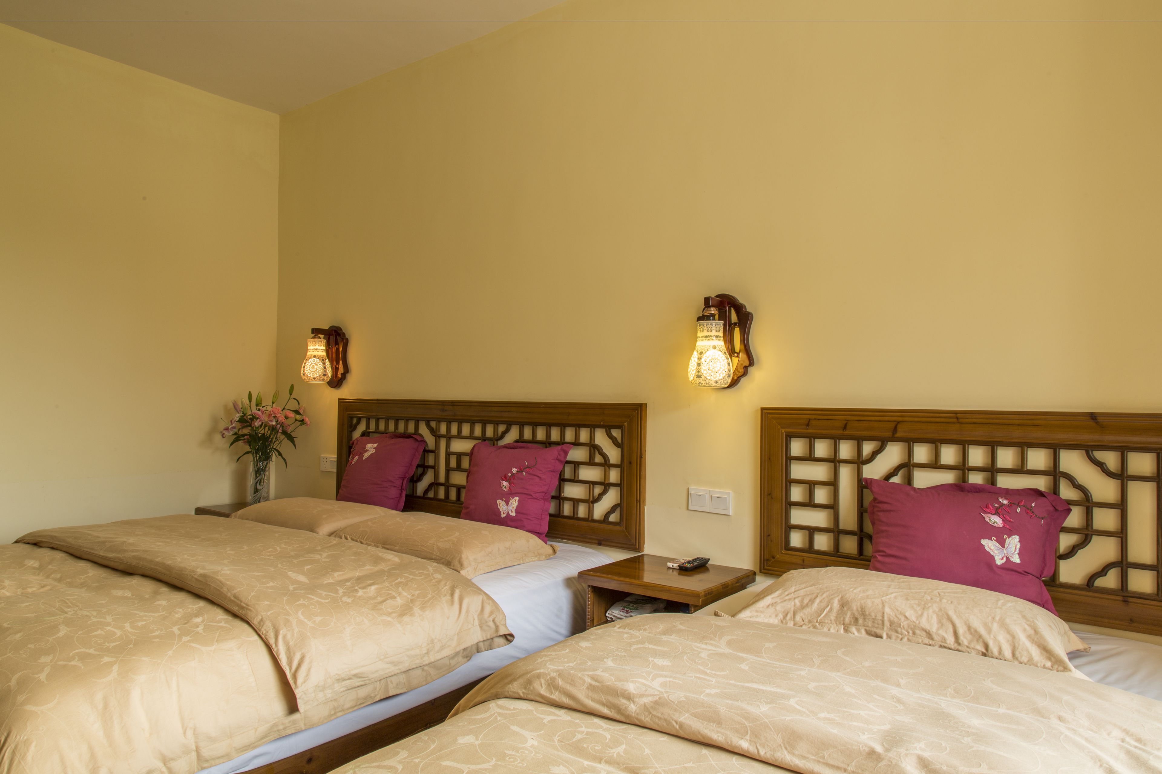 Habitación de hotel con tres camas, cada una con ropa de cama color beige y almohadas decorativas. Hay apliques de pared que proporcionan luz ambiental.