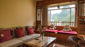 Una habitación acogedora con detalles de madera, un sofá con cojines rojos, una mesa con un jarrón de flores y dos osos de peluche en el alféizar de una ventana.