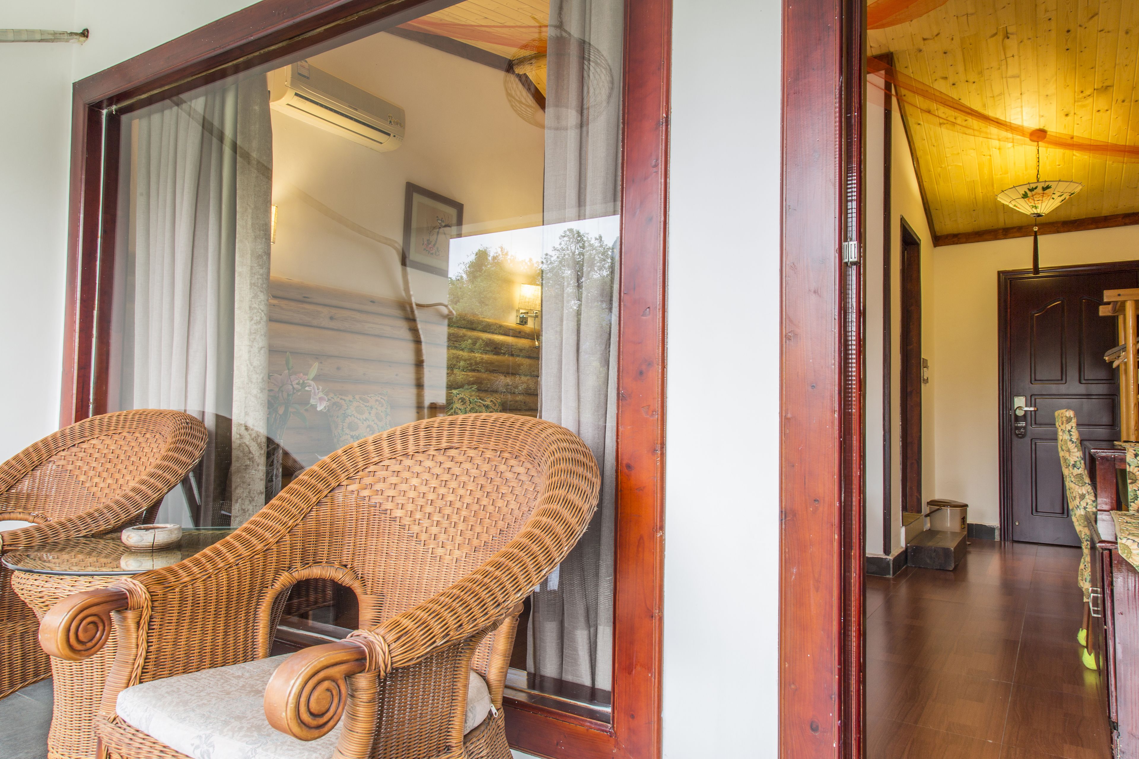 Wicker chairs near a glass door, a wooden floor, and a staircase leading to an upper level.
