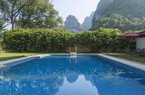 A swimming pool with clear blue water, surrounded by lush greenery and mountains in the background.