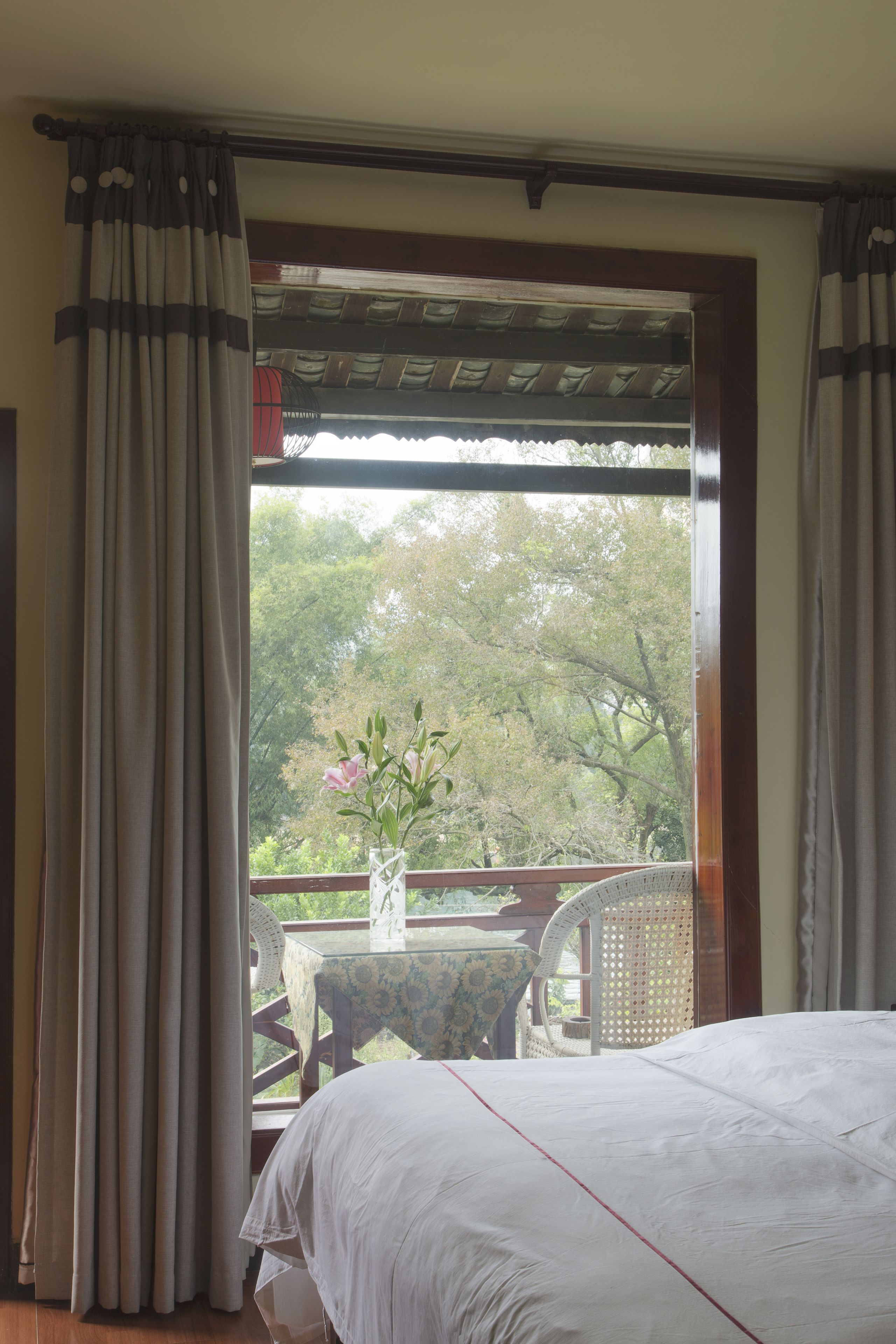 Un dormitorio con un ventanal grande, una cama, una mesa con un florero y una silla.