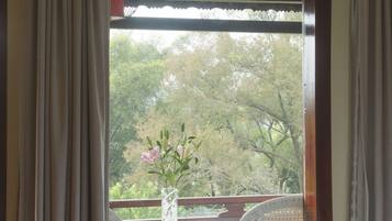Un dormitorio con un ventanal grande, una cama, una mesa con un florero y una silla.