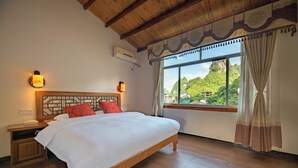 Un dormitorio con una cama de madera, dos mesitas de noche, una lámpara de noche, una ventana con cortinas y vistas al verdor exterior.