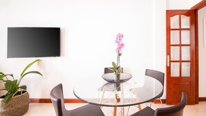 A room with a round glass table, four chairs, a potted plant, a flat-screen TV, and a wooden door.