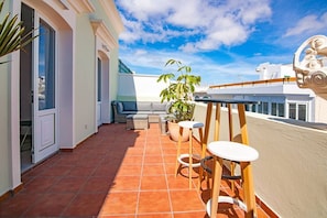 A balcony with a tiled floor, a sofa, two chairs, and potted plants.