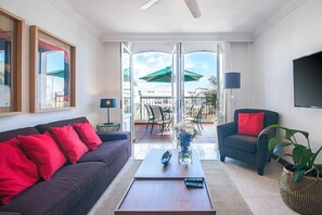 A modern living room with a sofa, armchair, coffee table, and a view of an outdoor balcony with chairs and umbrellas. - Rooms & Suites Terrace 4C, Arrecife, Lanzarote (Arrecife)