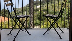 Duas cadeiras dobráveis numa varanda com guarda-corpo de metal, com vista para uma paisagem acidentada coberta por vegetação e alguns edifícios ao longe.