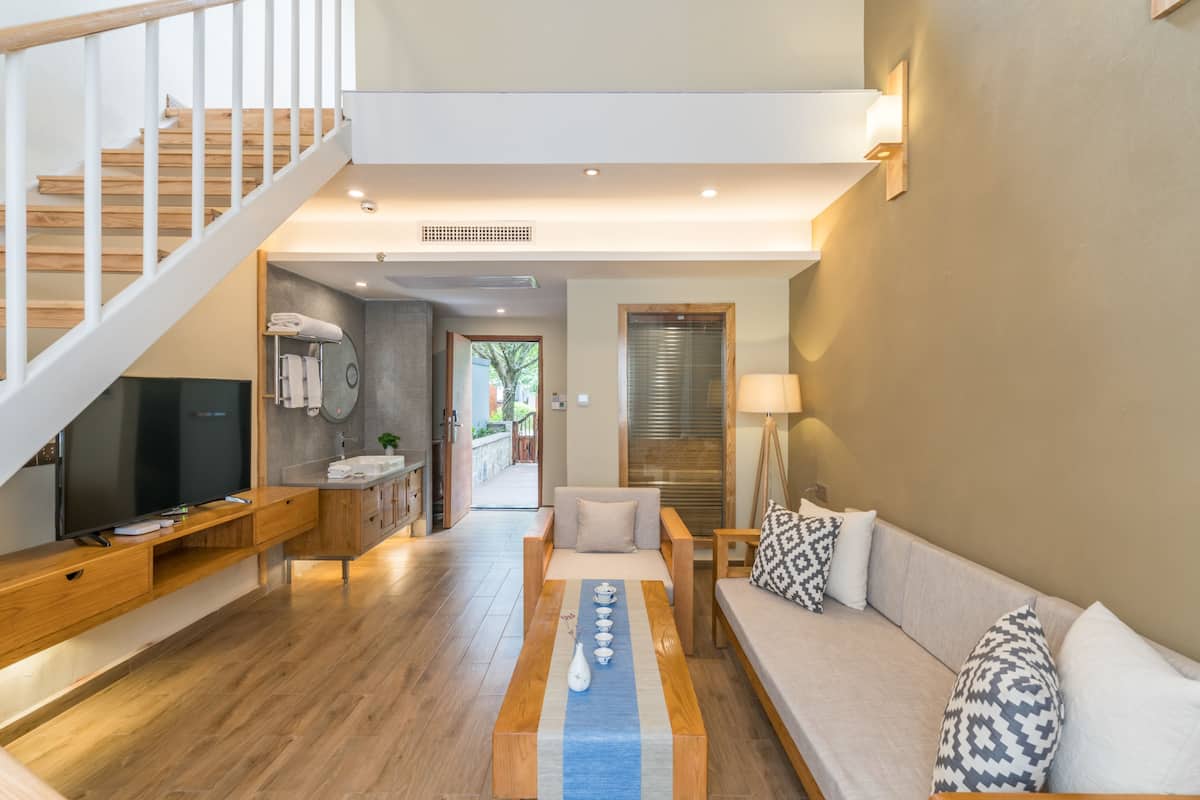 A modern living room with a wooden staircase, a sofa set, a coffee table, and a television.