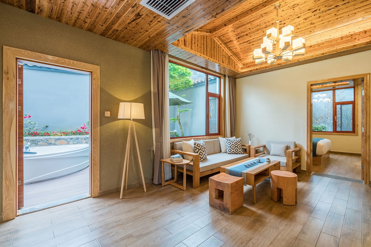 A spacious living area with a wooden ceiling, a sofa set, a coffee table, and a side table with a lamp.