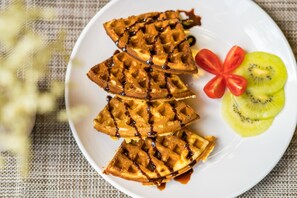 Une assiette avec des gaufres, des tranches de kiwi et des tranches de tomate.