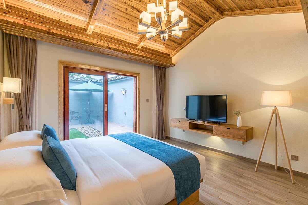 A bedroom with a large bed, a TV, and a wooden ceiling.