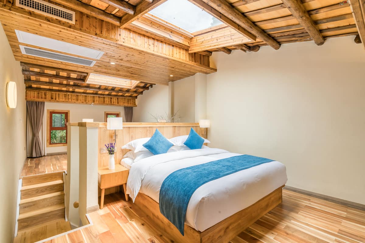 A wooden bedroom with a skylight, a bed with blue bedding, and a nightstand with a lamp.