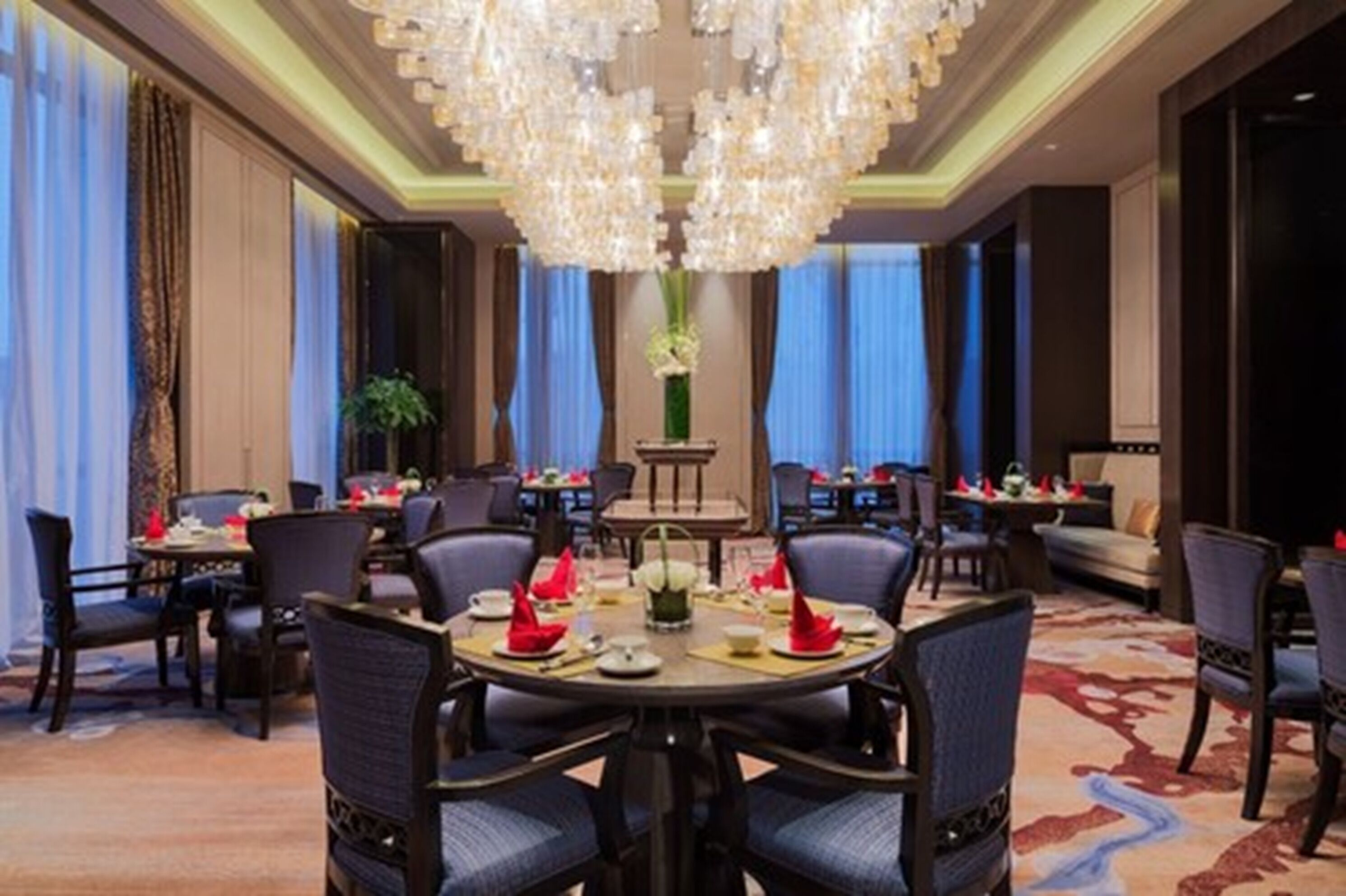 A hotel dining area with round tables set for a meal, surrounded by chairs.